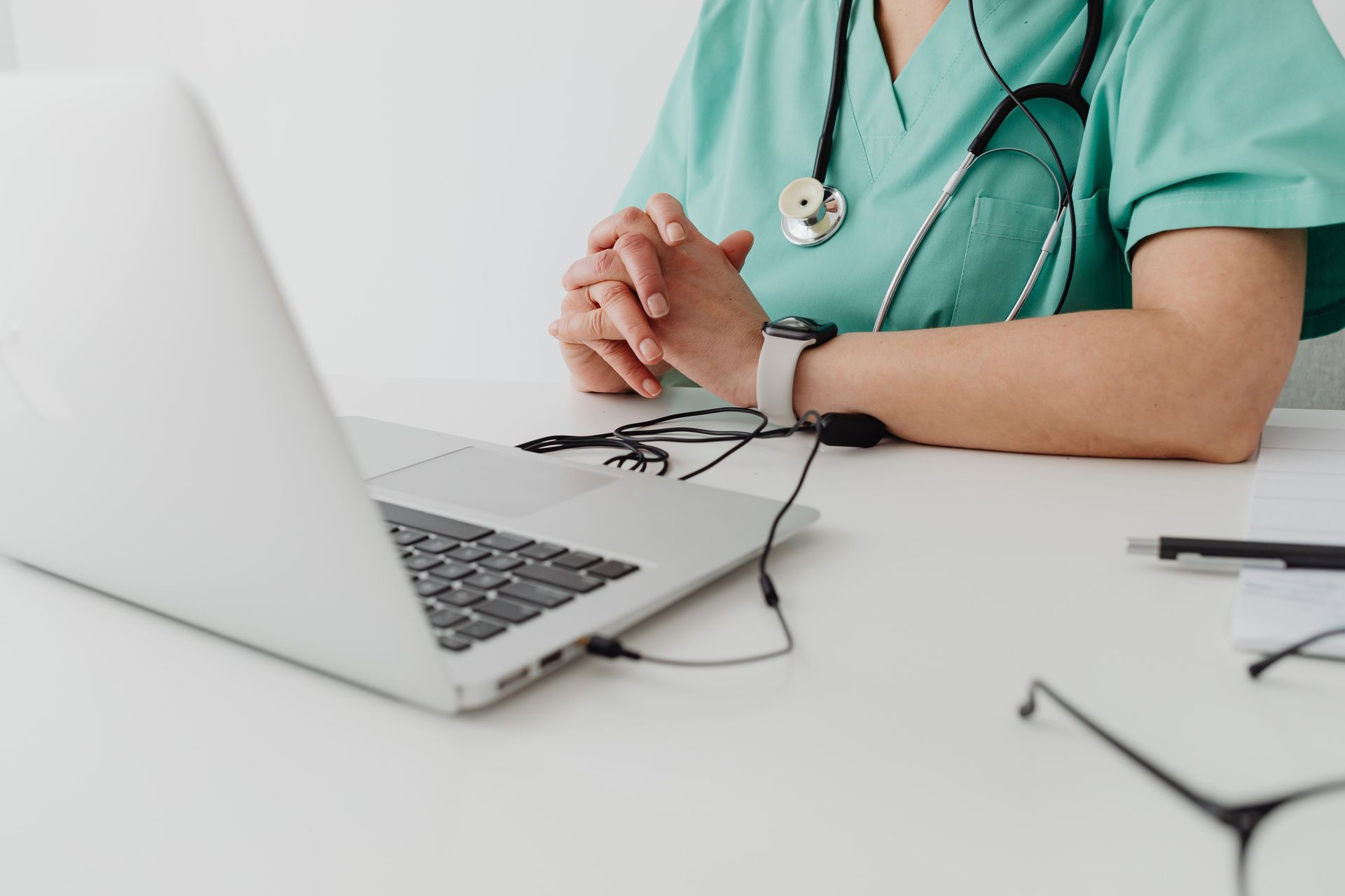 Medical practitioner in scrub suit using a laptop for remote consultation and documentation.